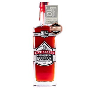The Fifty Best Flavored Whiskey Silver 2022 medal and Bartender Spirit Award bronze medal sit over a rectangular tall bottle with two gray labels spanning across all sides of the bottle with a white background. Hand-dipped pearlescent firetruck red wax drapes over the cork and neck of the bottle. An illustration of a firefighter in full protective gear with a fire ax is behind the words “Five Alarm Cinnamon Flavored Bourbon Whiskey”. The 1350 Distilling logo is centered at the top label.