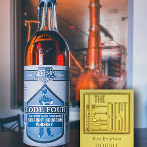 Double Gold Medal for The Fifty Best Bourbon 2023 sits to the left of a round bottle with gray label  in front of the "rocket still" in background. Hand-dipped silver wax drapes over the cork and neck of the bottle. An illustration of a police officer standing with arms crossed is behind the words “Code Four 115 Proof Cask Strength Straight Bourbon Whiskey”. The 1350 Distilling logo is centered at the top label.