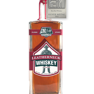 Silver Medal for The Fifty Best Rye Whiskey of 2022 sits over a rectangular tall bottle with two U.S. Marine Corp red labels spanning across all sides of the bottle with a white background. Hand-dipped U.S. Marine Corp red wax drapes over the cork and neck of the bottle. An illustration of a U.S.M.C. Drill Instructor sits behind the words “Leatherneck Rye Whiskey”. The 1350 Distilling logo is centered at the top label.