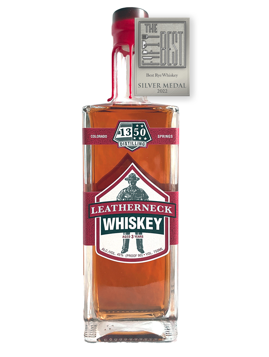 Silver Medal for The Fifty Best Rye Whiskey of 2022 sits over a rectangular tall bottle with two U.S. Marine Corp red labels spanning across all sides of the bottle with a white background. Hand-dipped U.S. Marine Corp red wax drapes over the cork and neck of the bottle. An illustration of a U.S.M.C. Drill Instructor sits behind the words “Leatherneck Rye Whiskey”. The 1350 Distilling logo is centered at the top label.