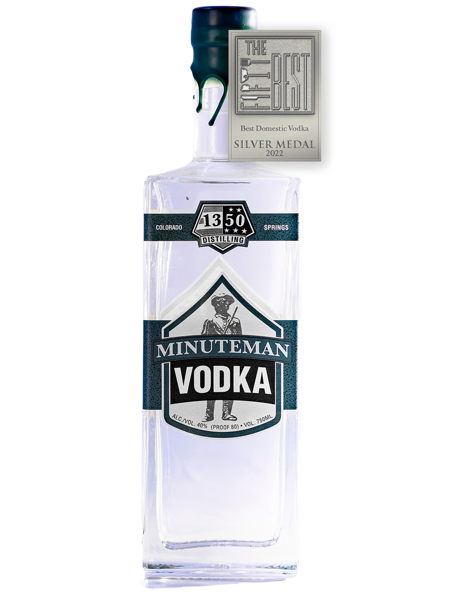 Silver Medal for The Fifty Best Domestic Vodka of 2022 sits over a rectangular tall bottle with two Army green labels spanning across all sides of the bottle with a white background. Hand-dipped army green wax drapes over the cork and neck of the bottle. Illustration of a U.S. Revolutionary soldier from the U.S. Revolution sits behind the words “Minuteman Vodka”. The 1350 Distilling logo is centered at the top label.
